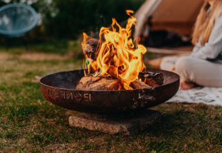 Vuurkorf bij tent op REBL Outdoor vakantiepark in Friesland, Nederland, met persoon op matje buiten.