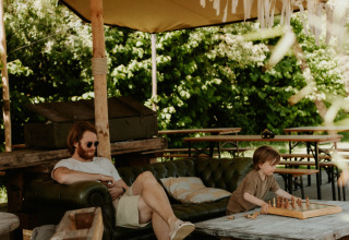 Man en kind ontspannen zich onder een tent in REBL Outdoor vakantiepark, Friesland, Nederland, terwijl ze schaken.
