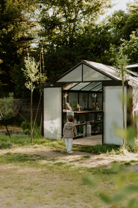 Et barn står uden for et drivhus i en grøn have ved REBL Outdoor feriepark i Friesland, Nederlandene.
