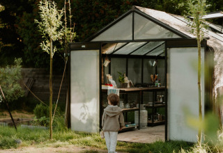Et barn står uden for et drivhus i en grøn have ved REBL Outdoor feriepark i Friesland, Nederlandene.
