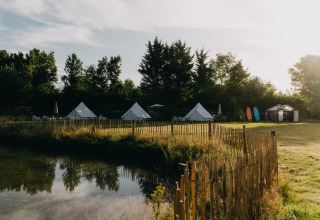 Parque de vacaciones soleado con tiendas, estanque, valla y árboles en REBL Outdoor en Friesland, Países Bajos.
