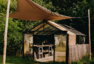 Et drivhus med solsejl i en feriepark omgivet af grønt, taget i REBL Outdoor i Friesland, Nederlandene.
