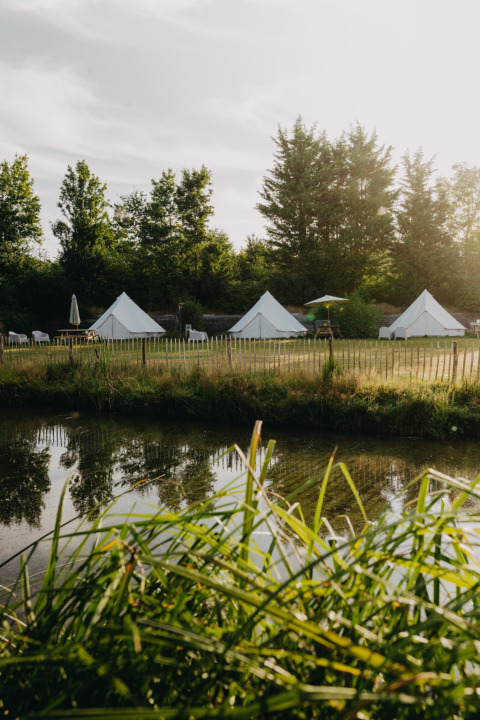 Tende glamping vicino a un laghetto circondate da alberi nel parco vacanze REBL Outdoor in Frisia, Paesi Bassi.