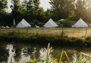 Glamping-Zelte am Wasser, umgeben von Bäumen bei Sonnenuntergang im REBL Outdoor Ferienpark Friesland, Niederlande.