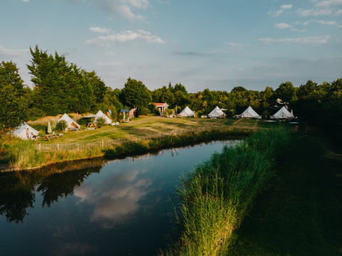 Zicht op REBL Outdoor vakantiepark in Friesland, Nederland met tenten, groen gras en een rustige vijver.