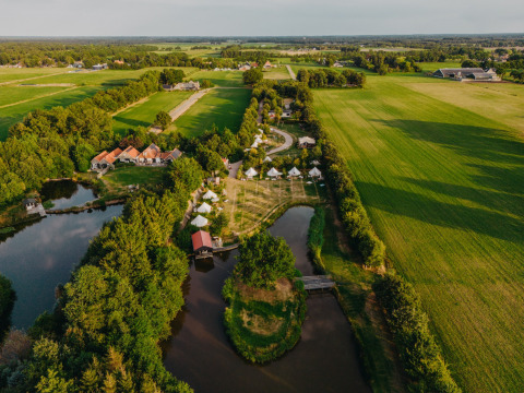 Vista aerea del parco vacanze REBL Outdoor in Frisia, Paesi Bassi, con tende, stagni e campi verdi intorno.