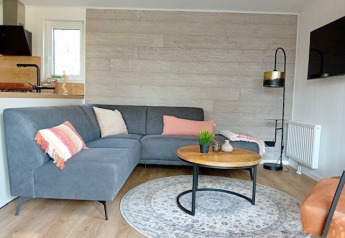 Moderne stue i Forest Lodge De Mooie Plek i Bospark Markelo, med grå sofa og rundt sofabord.