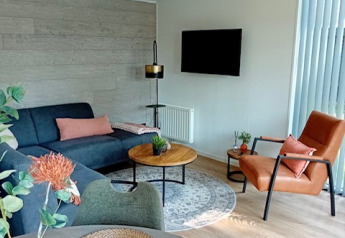 Moderne stue i Forest Lodge De Mooie Plek, Bospark Markelo, med sofagruppe, tv og naturlige toner.