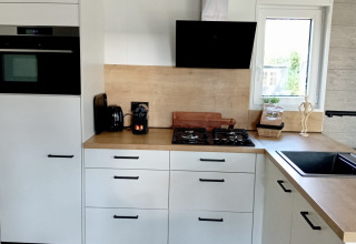 Modern white kitchen with wooden countertops and gas stove at Forest Lodge De Mooie Plek, Bospark Markelo.