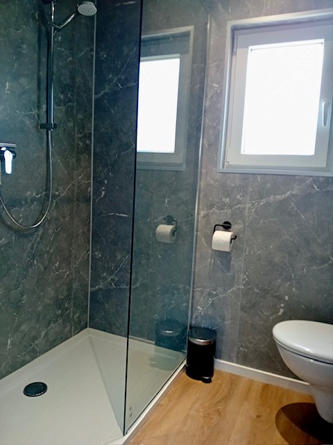 Baño moderno con ducha, inodoro y ventana en Forest Lodge De Mooie Plek, Bospark Markelo, Países Bajos.