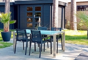 Udendørs terrasse med moderne borde og stole foran en sort træhytte på Forest Lodge De Mooie Plek i Holland.