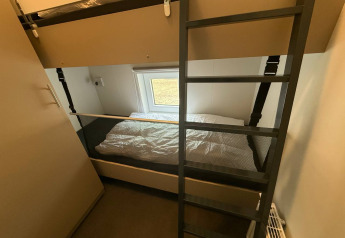 A room with a bunk bed, ladder and window inside Wood Cottage at Holiday park De Witte Berg, Netherlands.