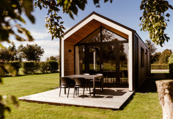 Moderne tiny house med træterrasse og bord i solrig have ved Holiday park Eigen Wijze, Holland.