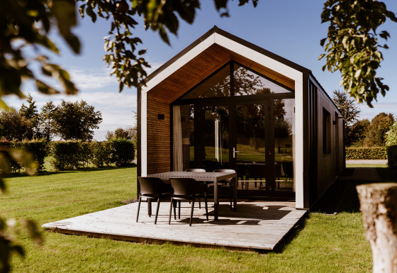 Moderne tiny house med træterrasse og bord i solrig have ved Holiday park Eigen Wijze, Holland.