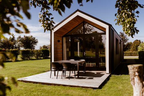 Modernes Tiny House mit Holzterrasse und Gartentisch im Holiday Park Eigen Wijze in den Niederlanden.