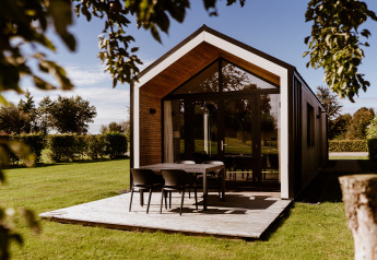 Modernes Tiny House mit Holzterrasse und Gartentisch im Holiday Park Eigen Wijze in den Niederlanden.