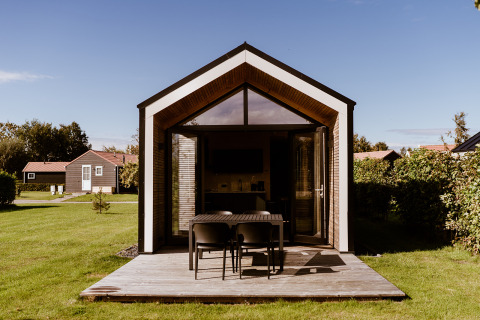 Tiny house moderna con terraza de madera en Holiday park Eigen Wijze, Países Bajos, rodeada de césped verde.