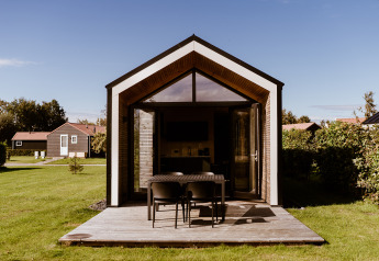 Tiny house moderna con terraza de madera en Holiday park Eigen Wijze, Países Bajos, rodeada de césped verde.