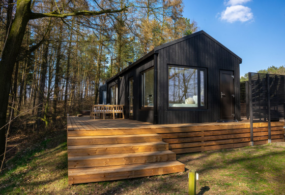 Koya Tiny Cabin en Wilsumer Berge, Alemania, cabaña negra moderna con terraza de madera rodeada de bosque.