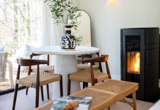 Moderne spiseplads med træstole, hvidt rundt bord, sort vase og pejs i Koya Tiny Cabin, Wilsumer Berge.