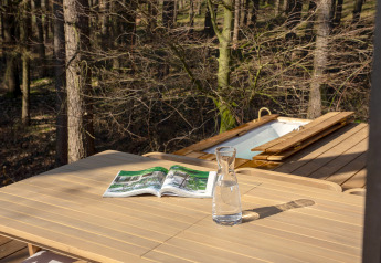 Buitentafel van hout met karaf water en tijdschrift, bos en bad bij Koya Tiny Cabin, Wilsumer Berge, Duitsland.