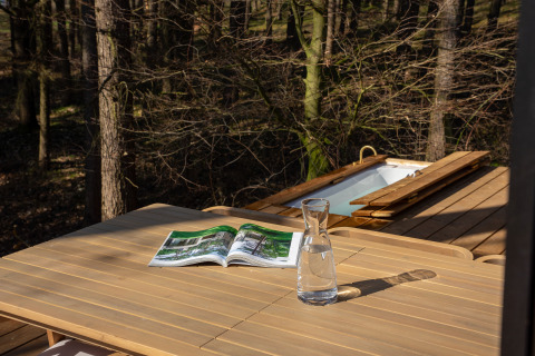 Holztisch mit Karaffe und Magazin auf Terrasse im Wald, Koya Tiny Cabin im Wilsumer Berge, Deutschland.