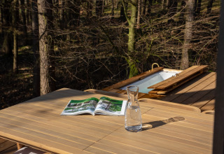 Holztisch mit Karaffe und Magazin auf Terrasse im Wald, Koya Tiny Cabin im Wilsumer Berge, Deutschland.