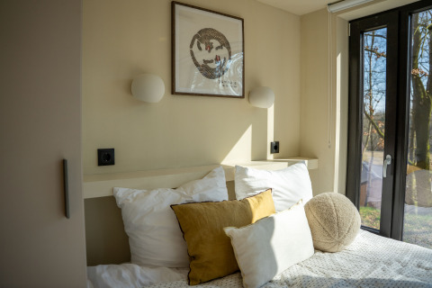 Slaapkamer met lichtinval en kussens in Koya Tiny Cabin bij Wilsumer Berge, Duitsland, grote ramen.