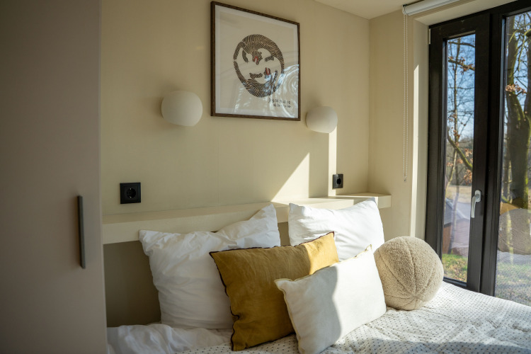 Sunny bedroom with pillows in Koya Tiny Cabin at Wilsumer Berge, Germany, featuring large windows.