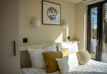 Camera luminosa con cuscini nella Koya Tiny Cabin a Wilsumer Berge, Germania, con grandi finestre.