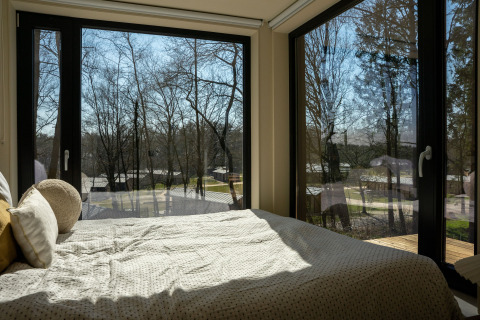 Bedroom at Koya Tiny Cabin in Wilsumer Berge, Germany, with large windows offering a forest view.