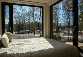 Camera da letto nella Koya Tiny Cabin a Wilsumer Berge, Germania, con ampie finestre e vista bosco.