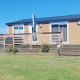 Een houten lodge met verhoogd terras, gelegen in open graslanden en omgeven door een blauwe lucht.