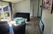 Salon d’un lodge au Camping Seasonova Les Vosges du Nord avec canapé, fauteuils et vue sur la terrasse.