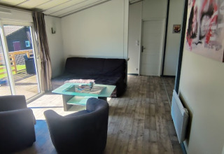 Wohnzimmer einer Lodge im Camping Seasonova Les Vosges du Nord mit Sofa, Sesseln und Terrassenblick.