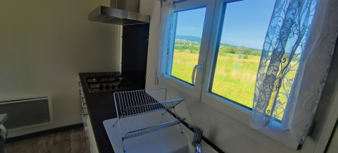 Keuken met gaskookplaat en weids uitzicht op groen veld aan het raam van de lodge op Camping Seasonova Les Vosges du Nord.