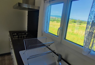 Küche mit Gasherd und Blick auf grüne Wiese durch das Fenster der Lodge im Camping Seasonova Les Vosges du Nord.