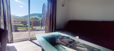Sala luminosa en lodge con mesa de cristal y vista a las montañas en Camping Seasonova Les Vosges du Nord.
