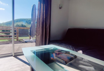 Salon lumineux d’un lodge avec table en verre et vue sur les montagnes, Camping Seasonova Les Vosges du Nord.