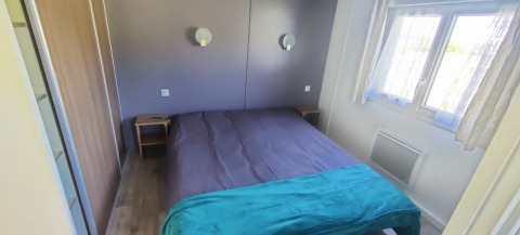 Dormitorio con cama doble, dos mesitas, ventana con cortinas y lámparas de pared en una cabaña en Francia.