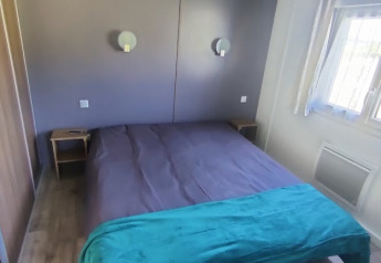 Dormitorio con cama doble, dos mesitas, ventana con cortinas y lámparas de pared en una cabaña en Francia.