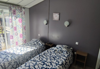 Tweepersoonskamer met twee aparte bedden, veelkleurige gordijnen en terras in een lodge in Frankrijk.