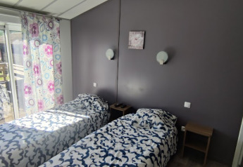 Tweepersoonskamer met twee aparte bedden, veelkleurige gordijnen en terras in een lodge in Frankrijk.
