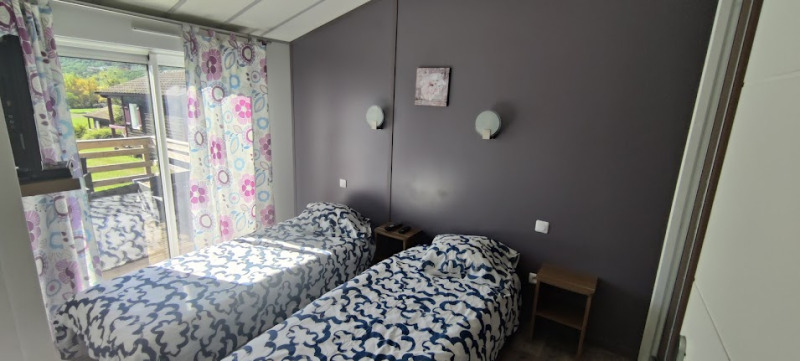 Tweepersoonskamer met twee aparte bedden, kleurrijke gordijnen en terras in een lodge in Frankrijk.