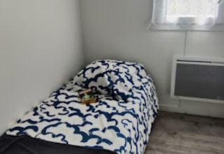 Helles Zimmer mit Einzelbett, schwarz-weißer Bettdecke, Fenster und Holzboden im Camping Seasonova.