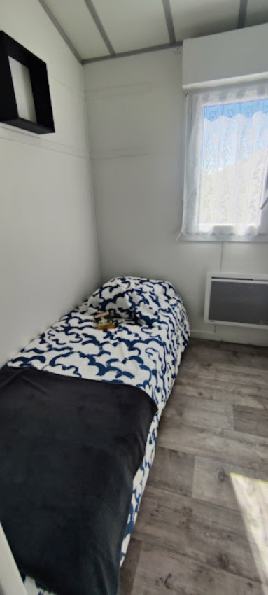 Helles Zimmer mit Einzelbett, schwarz-weißer Bettdecke, Fenster und Holzboden im Camping Seasonova.