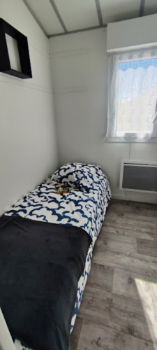 Lichte kamer met eenpersoonsbed, wit-blauw beddengoed, raam en houten vloer bij Camping Seasonova.