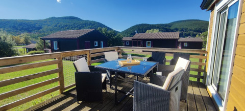 Sonnige Terrasse mit Esstisch und Stühlen in der CRL 1/5 Pers.-Lodge im Camping Seasonova Les Vosges du Nord, Frankreich.