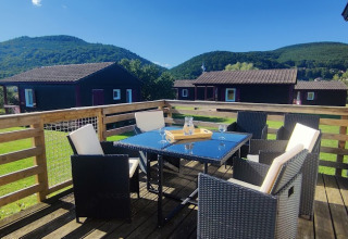 Sonnige Terrasse mit Esstisch und Stühlen in der CRL 1/5 Pers.-Lodge im Camping Seasonova Les Vosges du Nord, Frankreich.
