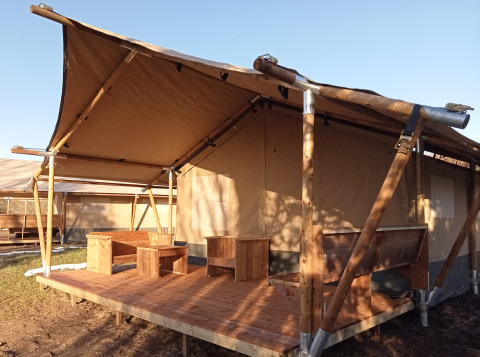Tenda safari con veranda in legno e area salotto esterna, ideale per un'esperienza di campeggio.